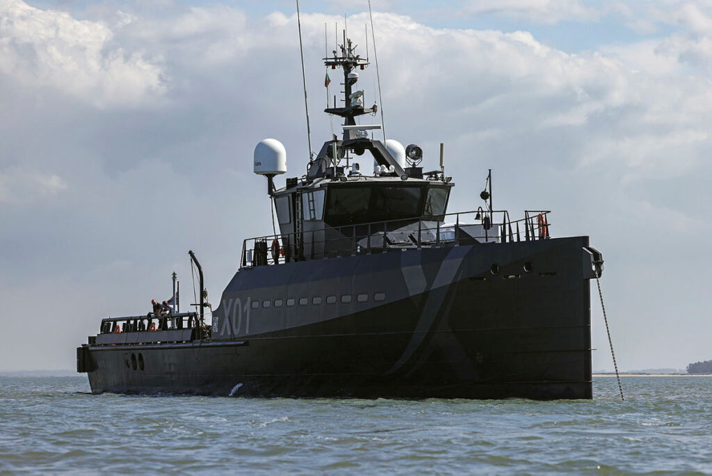 Pictured: XV Patrick Blackett at anchor in Portugal during Exercise REPMUS24. A range of drones and uncrewed vessels were deployed on a major international exercise in Portugal as the Royal Navy looks to push its latest technology to its limits. Autonomous Pacific 24 ribs, hand-launched drones, mini quadcopters and surveillance drones will join specially designed shipping containers and experimentation vessel XV Patrick Blackett for NATO’s annual uncrewed wargames. UK personnel joined with those from 26 other nations for the exercise, known as REPMUS, in Troia, southern Portugal, which focusses on uncrewed systems and looks to take kit and equipment from test phases to integration into operations and task groups. XV Patrick Blackett acted act as a test bed for elements of the trials and testing and embarked a range of technologies – building on its successes during last year’s exercise. The Royal Navy has also been testing uncrewed aerial vehicle Peregrine; surveillance drones Puma and Ebee Vision; uncrewed aerial systems Rotron and a remote-piloted seaboat. The Navy’s Office for Chief Technology Officer (OCTO) also sent NavyPODS – specially-designed shipping containers – which will act as operations rooms, extra storage space for the drones and as command centres. For the first time, this year’s annual exercise will also contribute to progress under AUKUS, the UK’s flagship defence and security partnership with Australia and the US. XV Patrick Blackett (X01) is an experimental ship used by the Royal Navy as a testbed for new technologies, including unmanned underwater vehicles, unmanned surface vehicles and quantum navigation.